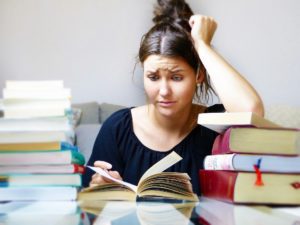 woman reading book with puzzled look on her face. books are surrounding her.